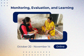 two females sitting on the ground, the female on the left is discussing the content of the document laid on the ground between the two people.